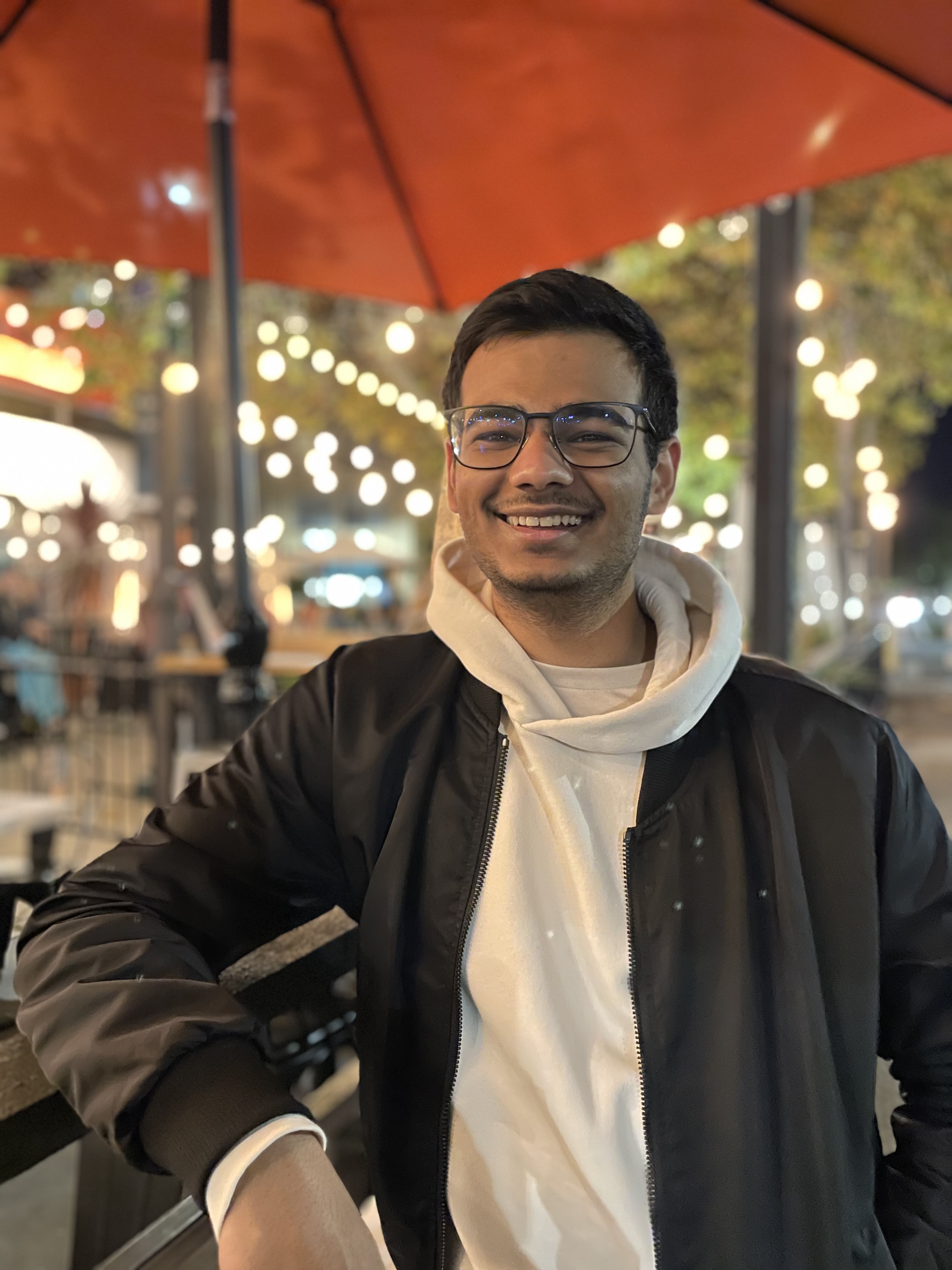 Karan, smiling under a cafe umbrella at night